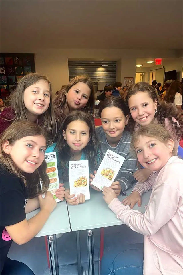 Students smiling while holing up facts about cauliflower and recipe card